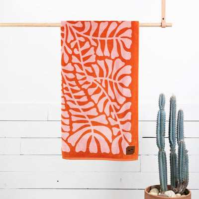 Jacquard beach towel in orange and pink with geometric pattern hanging indoors near cactus.